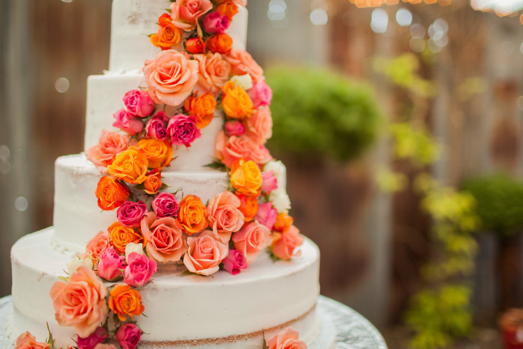 A tall wedding cake decorated with orange and pink flowers - fake wedding cakes