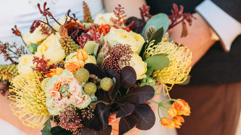 A bridal bouquet of yellow, burgundy and orange flowers for an autumn wedding.