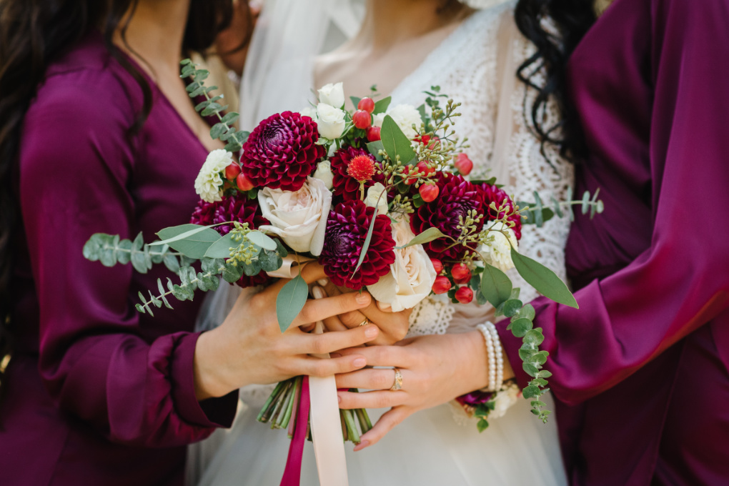A bride with rustic bouquet and bridesmaids in autumnal tones of deep red - how to plan an autumn wedding